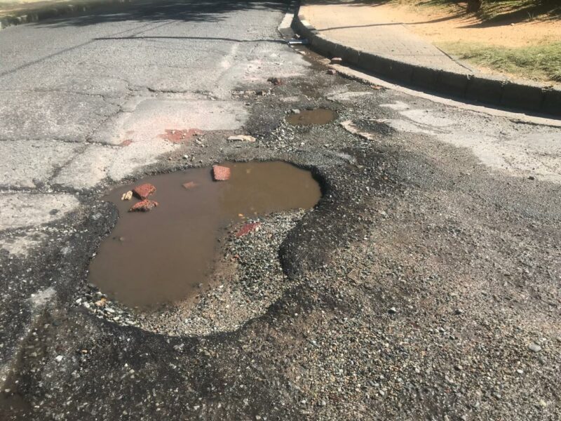 The potholes in the middle of the road force cars to swerve to avoid them, risking damage and accidents.