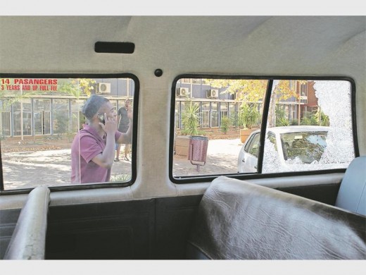 A driver describes his ordeal to someone on the phone whilst walking past the shattered window of a taxi in front of the Middelburg police station.