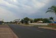 Wide street lined with palm trees and residential homes under a cloudy sky. The empty road and overcast weather evoke a calm, serene mood.