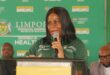 A woman in a green shirt speaks into a microphone at a podium against a backdrop reading "Limpopo Department of Health." The setting is formal and focused.
