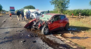 A red car with severe front-end damage is on a rural road, involved in an accident. Emergency responders and bystanders are present, creating a tense scene.