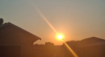 Sunset over a suburban neighborhood, with silhouettes of houses and trees. The sun's warm glow creates a tranquil, peaceful atmosphere.