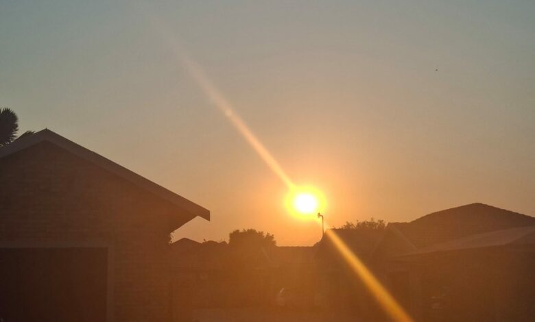 Sunset over a suburban neighborhood, with silhouettes of houses and trees. The sun's warm glow creates a tranquil, peaceful atmosphere.