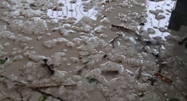 A soaked patio with white hailstones scattered across wet tiles. Twigs, leaves, and debris are interspersed, evoking a chaotic aftermath of a storm.