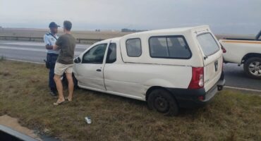 Accident scene where a policeman and a man is standing next to the vehicle which was in the accident.