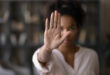 A person with an outstretched hand facing the camera, signaling stop. The background is blurred, and the mood conveys seriousness and assertiveness.