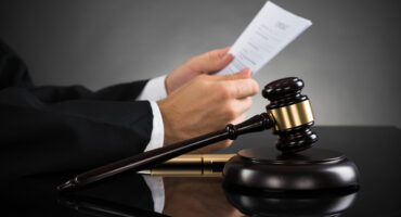 A judge's hands holding papers above a wooden gavel on a desk, conveying a sense of authority and legal proceedings in a courtroom setting.