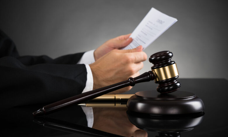 A judge's hands holding papers above a wooden gavel on a desk, conveying a sense of authority and legal proceedings in a courtroom setting.