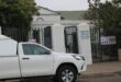 A white pickup truck parked outside a gated entrance marked "Magistrate Court." Signs indicate a construction site nearby. The scene is overcast.