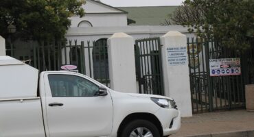 A white pickup truck parked outside a gated entrance marked "Magistrate Court." Signs indicate a construction site nearby. The scene is overcast.