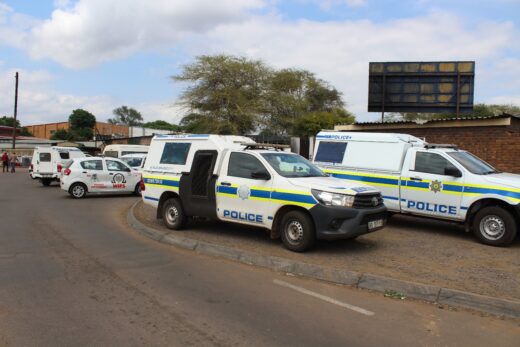Several police vehicles, including SUVs and vans with blue and yellow stripes, are parked on a street, conveying a sense of official presence.