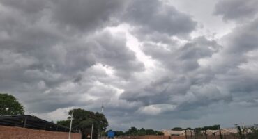 Dark, dramatic storm clouds fill the sky over a rural road with a single vehicle in the distance. The scene evokes a sense of anticipation and calm before a storm.