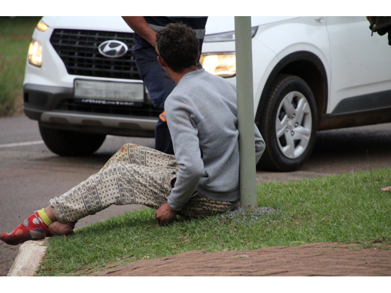 Drug addict sitting against a pole while people trying to calm him down.