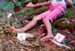 The image depicts a crime scene in a forest. A person lies on the ground wearing pink shorts, surrounded by evidence markers and a knife. The tone is tense and mysterious.