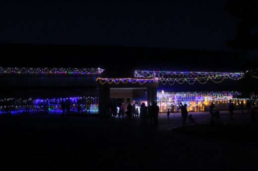 Dark evening scene with a building adorned in colorful string lights. Silhouettes of people gather beneath the festive, illuminated decorations. Festive ambiance.