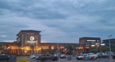 Shopping center at dusk with lit signs for Groblersdal Mall, Woolworths, and McDonald's. Cars parked in the lot, under a cloudy sky, creating a calm atmosphere.