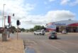 A sunny day at an intersection with cars driving near a Cashbuild store. Traffic lights are visible, but not working. The sky is partly cloudy, creating a calm atmosphere.
