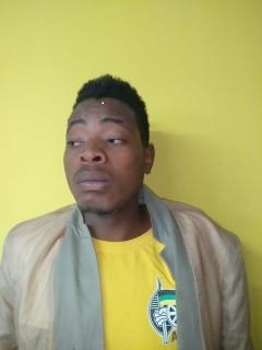 A man in a yellow shirt and beige jacket stands against a matching yellow background, looking contemplative and sideways with a serious expression.