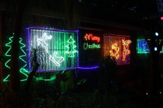 Neon Christmas lights on a building display trees, reindeer, and a "Merry Christmas" sign. The festive glow creates a joyful holiday atmosphere.