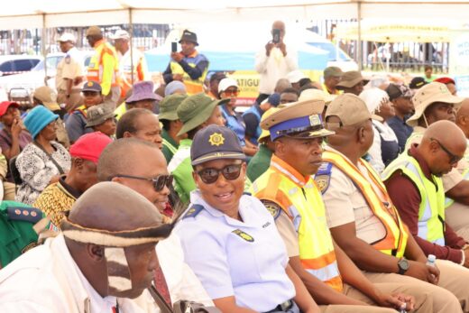 A diverse group of people, including police officers in uniform and others in casual attire, seated under a tent. The setting appears to be a public event, with a focus on community engagement and safety. The atmosphere is attentive and organized.