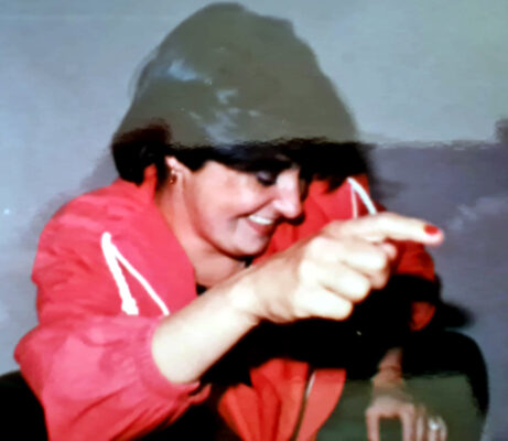 Woman in a red jacket smiling joyfully, pointing forward. Her expression conveys happiness and playfulness, creating a lively atmosphere.