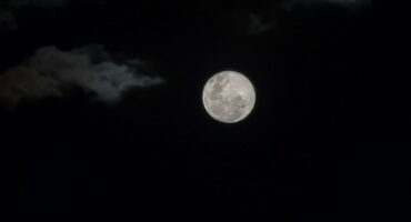 Full moon shining brightly in a dark night sky, surrounded by scattered clouds. The mood is serene and ethereal, highlighting the moon's glowing presence.