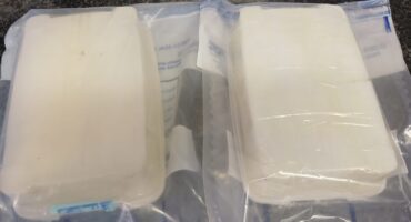 Two rectangular packages wrapped in transparent plastic lie side-by-side on a granite countertop. The packages appear vacuum-sealed and contain a solid, white substance.