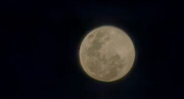 Full moon glowing brightly against a dark, clear night sky, emphasizing its craters and texture. The scene conveys a serene, tranquil mood.