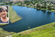 A serene lake surrounded by lush greenery and houses, reflecting a clear blue sky. Inset shows a smiling woman with short gray hair, adding warmth.