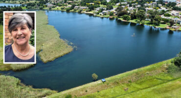 A serene lake surrounded by lush greenery and houses, reflecting a clear blue sky. Inset shows a smiling woman with short gray hair, adding warmth.