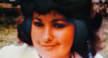 A close-up of a woman with dark hair and a gentle smile, wearing a white shirt. The background is blurred, creating a warm, nostalgic feel.