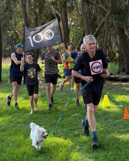 Douglas Franklin running his 100th parkrun. A man with his dog on a leash at the parkrun,.