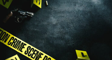 A revolver lies on a textured dark surface surrounded by yellow crime scene markers and tape, creating a tense and mysterious atmosphere.