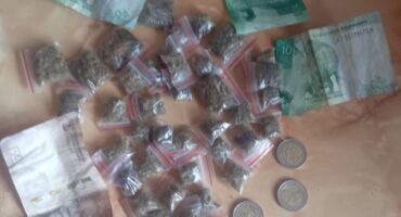 Small bags of dagga are arranged on a surface with various denominations of currency, including coins and folded bills, indicating a transactional context.