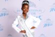 Young girl in a sparkly silver and white outfit with a crown, wearing a "Miss South Africa" sash, smiles confidently against a pageant backdrop.