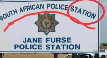 Sign for "South African Police Service" at Jane Furse Station. A red pen circles "STATION" with the police emblem in the center. A vehicle is visible behind.