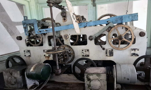 Complex machinery with interlocking gears and metal components, set against a light-colored background.