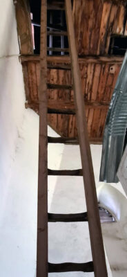 A wooden ladder leans against a rustic wooden ceiling inside a dimly lit room, creating a sense of intrigue and exploration.