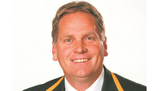 A smiling man in a suit with yellow and black trim on the lapels, against a plain white background. He appears confident and approachable.