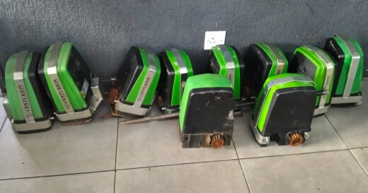 Nine green and black motor units are lined up against a gray wall on a tiled floor. A white electrical outlet is visible above them.