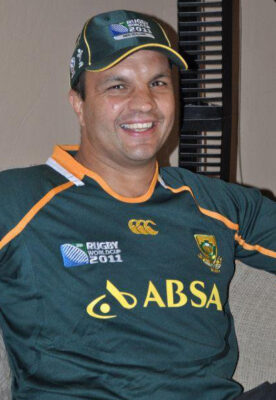 Man smiling while sitting, wearing a green rugby World Cup 2011 jersey and matching cap. He appears relaxed and cheerful, conveying a positive mood.