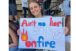 A woman smiles, holding a sign that reads "Ain't no liar! Ben's on fire" with bright red and blue letters, a flame, and a football. The mood is enthusiastic.