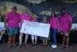 Six people stand smiling with a large ceremonial check for 150,000 rand, wearing matching pink shirts, in front of a fishing-themed banner.