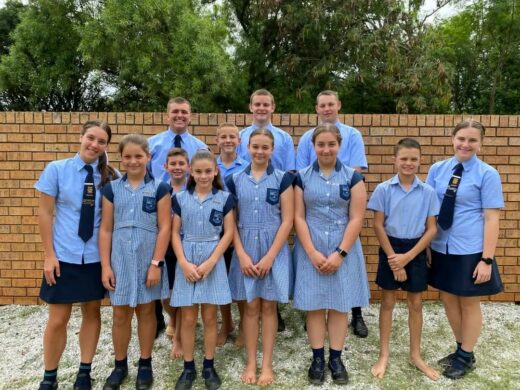 A group of eleven students in blue checkered and solid blue uniforms stand smiling against a brick wall, conveying a sense of unity and school spirit.