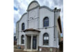 Historic synagogue with a white facade, arched windows, and a decorative entryway with columns. The sky is partly cloudy, conveying a serene atmosphere.