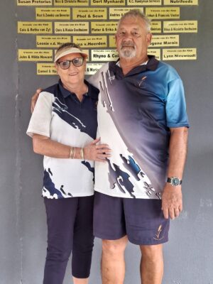 A couple in matching blue and white outfits smiles warmly. They stand in front of a wall with yellow name plaques, conveying a sense of camaraderie.