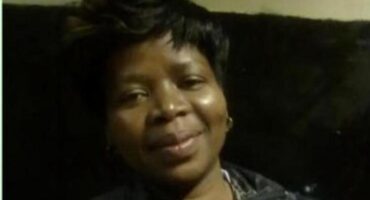 A person with short, dark hair smiles subtly against a dark background. The lighting is soft, creating a warm, welcoming atmosphere.