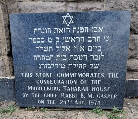 A commemorative stone plaque with Hebrew and English text, including a Star of David. It marks the consecration of Middelburg Taharah House on August 25, 1974, by Chief Rabbi B.M. Casper. The tone is respectful and solemn.