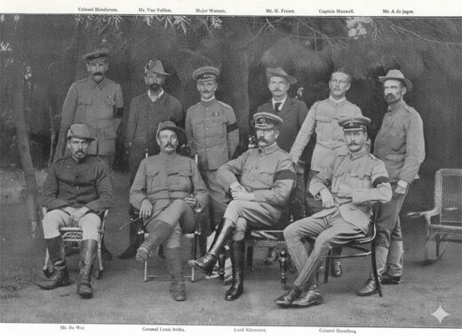Historic black-and-white photo of ten men in military uniforms, seated and standing, with serious expressions. Background features trees and outdoor shadows.