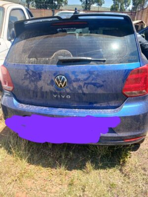 Rear view of a dusty blue Volkswagen Vivo parked on grass, next to another vehicle. The scene conveys a casual and slightly neglected feel.
